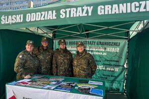  Namiot Straży Granicznej. Wewnątrz 4 uśmiechnięte funkcjonariuszki. Przed nimi na stoliku ulotki.