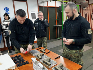 Strzelnica ŚLOSG. Na stole położone są cztery pistolety wiatrówki Glock 19. Dwóch funkcjonariuszy ładuje magazynki śrutem. Strzelnica ŚLOSG. Na stole położone są cztery pistolety wiatrówki Glock 19. Dwóch funkcjonariuszy ładuje magazynki śrutem.