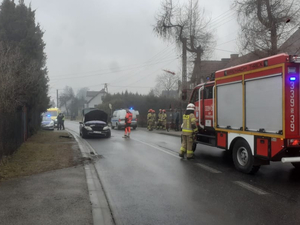 Jezdnia. Na prawym pasie samochód Straży Pożarnej, przy drzwiach kierowcy stoi strażak. Na lewym pasie uszkodzony pojazd, za nim po prawej i lewej stronie stoją radiowozy. Jezdnia. Na prawym pasie samochód Straży Pożarnej, przy drzwiach kierowcy stoi strażak. Na lewym pasie uszkodzony pojazd, za nim po prawej i lewej stronie stoją radiowozy.