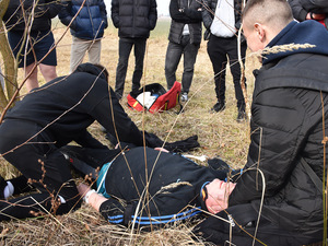 Ćwiczenia z udzielenia pierwszej pomocy przedmedycznej. Osoba położona jest na trawie, jedna z osób podtrzymuje jej głowę a druga zakłada opatrunek na prawa nogę. Ćwiczenia z udzielenia pierwszej pomocy przedmedycznej. Osoba położona jest na trawie, jedna z osób podtrzymuje jej głowę a druga zakłada opatrunek na prawa nogę.