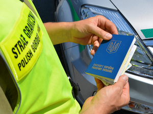 Funkcjonariusz w żółtej kamizelce. W rękach trzyma ukraiński paszport. Funkcjonariusz w żółtej kamizelce. W rękach trzyma ukraiński paszport.