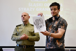 Od lewej st. chor. SG Mateusz Buchta, obok niego student trzymający kartkę z odbita dłonią. Na szyi ma założone słuchawki. Od lewej st. chor. SG Mateusz Buchta, obok niego student trzymający kartkę z odbita dłonią. Na szyi ma założone słuchawki.