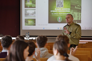 Sala wykładowa. Studenci siedzący na krzesłach. Przed nimi stoi por. SG Szymon Mościcki, za nim wyświetlona jest prezentacja. Sala wykładowa. Studenci siedzący na krzesłach. Przed nimi stoi por. SG Szymon Mościcki, za nim wyświetlona jest prezentacja.