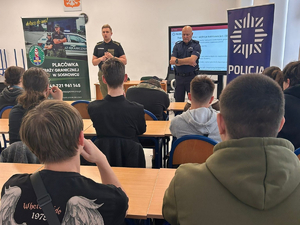  Funkcjonariusz Straży Granicznej i Policji podczas prelekcji. Obok nich banery. W ławkach młodzież Zespołu Szkół im. Mikołaja Kopernika w Sosnowcu