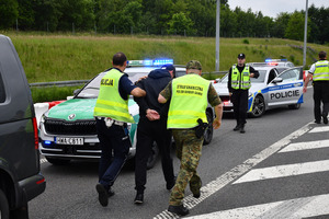  Funkcjonariusz Policji Straży Granicznej prowadza Zatrzymanego do radiowozu.