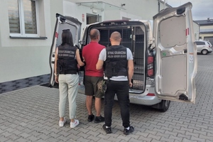  Funkcjonariuszka i funkcjonariusz Straży Granicznej prowadzą zatrzymanego do samochodu.