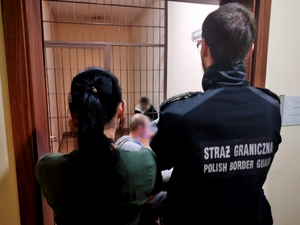 Funkcjonariusze SG stoją przed kratą, za nią osoba zatrzymana.
