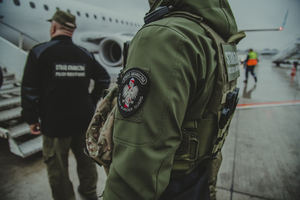 Pyta lotniska. Dwóch funkcjonariuszy Straży Granicznej, w tle samolot.