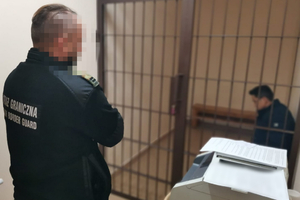  Funkcjonariusz Straży Granicznej, krata a za nią osoba zatrzymana