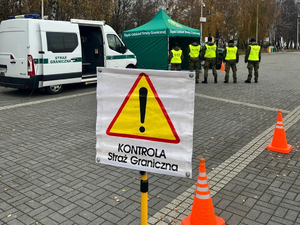  Samochód i namiot Straży granicznej, 5 funkcjonariuszy stojących tyłem, na pierwszym planie znak ostrzegawczy a pod nim napis &quot;Kontrola Straż Graniczna&quot;.