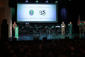 Obchody jubileuszu 35-lecia Śląskiego Oddziału Straży Granicznej. Wręczanie medali, odznaczeń państwowych i resortowych oraz aktów mianowani na kolejne stopnie służbowe w Straży Granicznej. Scena, osoba przemawiająca, dwoje prowadzących.
