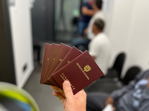  Zdjęcie poglądowe. Paszporty kolumbijskie trzymane w dłoni, w tle rozmyte sylwetki ludzi.